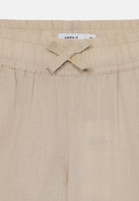 Vaaleanbeiget pellavahousut, joissa on joustava vyötärönauha ja edessä rusetti, hienovarainen tekstuuri sekä rento istuvuus.