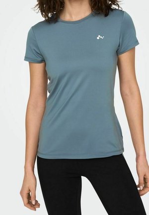 Femme portant un T-shirt de sport ajusté bleu clair à manches courtes avec un petit logo blanc sur la poitrine et des leggings noirs.