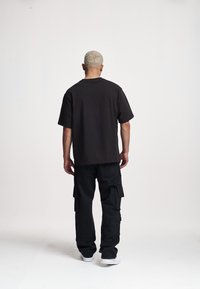T-shirt noir oversize à manches courtes, associé à un pantalon cargo noir avec de nombreuses poches, et des baskets blanches. Design simple.