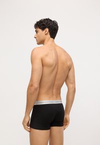 Los calzoncillos boxer negros presentan una cinturilla gris con el logo de "TOMMY HILFIGER". La tela parece suave, ajustándose perfectamente al cuerpo.