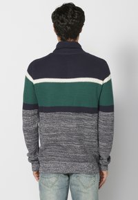 Sweter dzianinowy w paski w kolorze granatowym i zielonym, z wysokim kołnierzem, posiadający teksturowany splot oraz kontrastujące poziome pasy w kolorze białym i ciemnogranatowym.