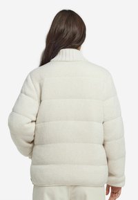 Witte pufferjack met een gestructureerde gebreide afwerking, geribde kraag en horizontaal doorgestikt patroon. Casual pasvorm met een zachte, gezellige uitstraling.