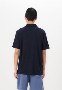 Ναυτικό κοντομάνικο πόλο μπλούζα με καρό σχέδιο και κανονικό γιακά, συνδυασμένο με ανοιχτό μπλε σορτσάκι. Λείο ύφασμα.