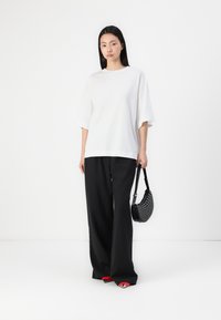 Witte oversized t-shirt met korte mouwen, gecombineerd met zwarte wijde broek en een zwarte handtas met stippen. Rode accenten op het schoeisel.