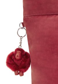 Bolsa de tela roja con una superficie texturizada y un llavero de mono de peluche en tonos rojos a juego, sujeto con un anillo y cadena de plata.
