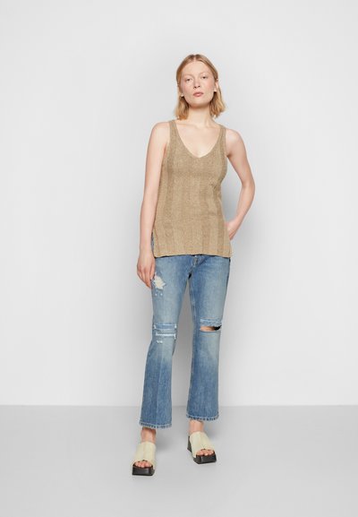 Top de malha bege com decote em V, combinado com jeans desgastados azul claro e sandálias de slide creme com plataforma preta.