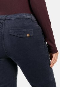 Donkerblauwe corduroy broek met een gestructureerde afwerking, voorzien van een klein bruin logo-label op de achterzak en een elastische tailleband.