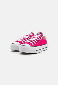 Sneaker basse in tela rosa con lacci bianchi, punta in gomma e suola testurizzata. Presenta una striscia nera di accento lungo il lato della suola.