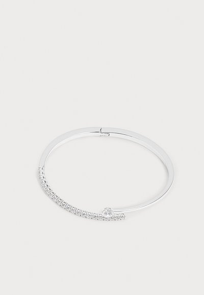 Bracelet jonc fin en argent avec une rangée de petites pierres claires taillées en carré et une pierre ronde plus grande près du fermoir sur fond blanc.