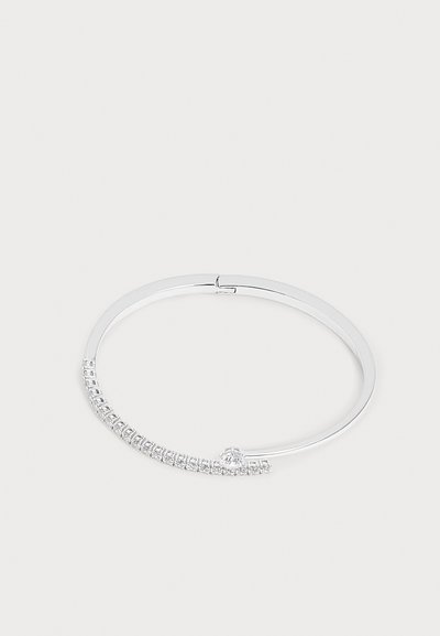 Bracelet jonc fin en argent avec une rangée de petites pierres claires taillées en carré et une pierre ronde plus grande près du fermoir sur fond blanc.