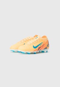 Para pomarańczowe korki piłkarskie Nike z niebieskim swooshem i akcentami, z sznurowadłami i formowanymi kołkami na białym tle.