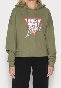 Olivově zelená crop mikina s kapucí na stahovací šňůrku, zdobená červeným trojúhelníkovým logem, bílým textem a kamínkovými akcenty na nápisu "ICON".