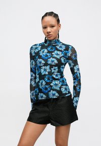 Garām piedurknēm tops ar melnu caurspīdīgu audumu, rotātu ar zilām ziedu rakstām; kopā ar melnām šortām ar punktētu tekstūru. Augsts apkakles dizains.