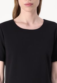Top nero a maniche corte con scollatura rotonda e texture liscia, realizzato in un tessuto leggero, con dettagli di cucitura sottili.