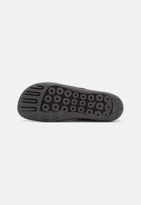 Semelle de chaussure noire avec des motifs circulaires antidérapants, trois lignes de bande de roulement horizontales au talon, et le nom de la marque "Camper" avec la taille 38 sur le côté.