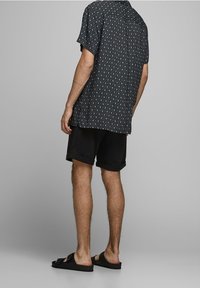 Svart kortärmad skjorta med vitt diamantmönster, tillsammans med svarta shorts och svarta sandaler; mjukt tyg och avslappnad passform.