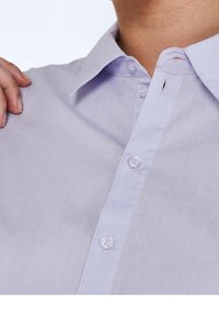 Camicia button-up di un leggero viola con colletto, caratterizzata da una texture liscia e bottoni abbinati. Ingrandimento dell'area del collo, che mostra i dettagli delle cuciture.