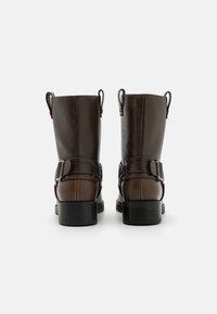 Bottines en cuir brun avec une finition mate, dotées de deux sangles ajustables, de languettes de traction et d'une semelle en caoutchouc noir robuste.