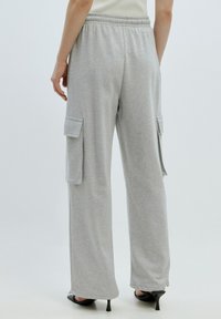 Grijze sweatpants met een ontspannen fit, voorzien van zijcargo pockets en een elastische tailleband. De stof lijkt zacht en textuur te hebben.