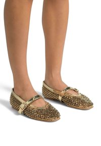 Chaussures plates dorées avec un dessus texturé en petits clous, dotées d'une bride sur le pied et d'un bout arrondi.