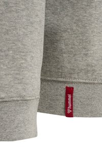 Grå sweatshirt-tyg med en mjuk, texturerad yta. Har en röd etikett vid nederkanten med märket "hummel" i vit text.