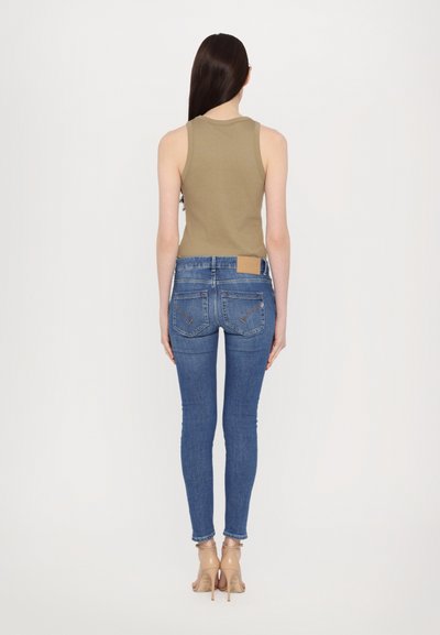 Top sin mangas en color caqui combinado con vaqueros ajustados azules. Los vaqueros tienen una etiqueta en la parte trasera, forma slim y un leve estiramiento. Llevado con tacones nude.
