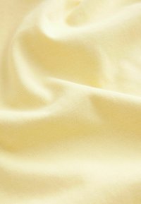 Světle žlutá látka, s hladkým povrchem, mírně elastická a s jemným ribkovým vzorem, zmačkaná a přehozená, aby ukázala svou jemnost.