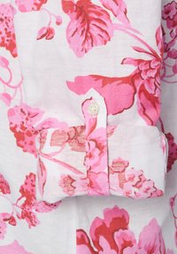 Blumenshirt mit weißem Hintergrund, auf dem große rosa und rote Blumen abgebildet sind. Mit Knopfmanschette, einem kleinen Knopf und Doppelnähten.