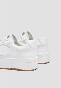 Ein Paar weiße Leder-Plateausneaker mit dicken Sohlen und braunem Profil auf einem hellgrauen Hintergrund.