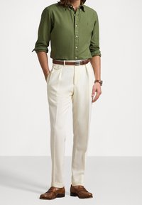 Zelená košile s knoflíky, zasunutá do krémových plisovaných kalhot. Hnědý kožený opasek a boty dokončují oblečení. Klasický střih, hladká textura.