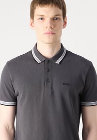Šahtas polo krekls ar teksturētu audumu, trīs pogām priekšpusē un kontrastējošu baltu svītru apkakli un piedurkņu galiem. Logo uz krūtīm.