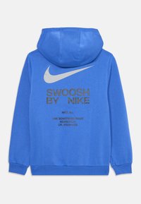Modra kapuča pulover iz mehkega blaga, z velikim sivo-nike simbolom in napisom na hrbtni strani. Sproščeni robovi na manšerah in ob hemu.