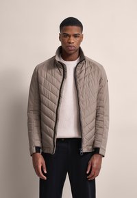 Leichtgewichtige Steppjacke in Taubengrau mit hohem Kragen, Reißverschluss und dunklen Akzenten. Verfügt über ein diagonales Steppmuster und elastische Bündchen.