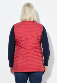 Rode gewatteerde puffer vest met chevronpatroon, voorzien van een rechte zoom en mouwloos ontwerp, gecombineerd met een marineblauw langetermijn T-shirt.