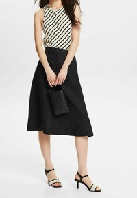 Falda midi negra combinada con una blusa sin mangas a rayas. Presenta una cintura ajustada, textura suave y tacones negros con tiras que tienen un acento de color claro.