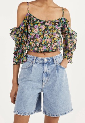 Woman wearing a floral off-shoulder ruffle blouse with thin straps and light blue high-waisted denim shorts with pockets.