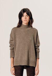 Übergrößen, olivgrüner Wollrollkragensweater mit gerippten Bündchen und Saum, präsentiert sich mit einer strukturierten Oberfläche und überschnittenen Schultern.