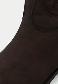 Κοντινό πλάνο σκούρου καφέ δερμάτινου μπότες με λεπτομερείς ραφές στο δάχτυλο και στο πάνω μέρος, με φόντο λευκό.