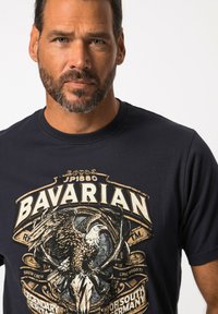 Námořnické bavlněné tričko s velkým, detailním grafikou orla se zlatými akcenty a textem "BAVARIAN". Design s kulatým výstřihem a krátkými rukávy.