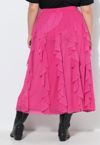 Falda larga rosa con volantes en capas, textura suave y cintura ajustada. Lleva botas negras con estampado.