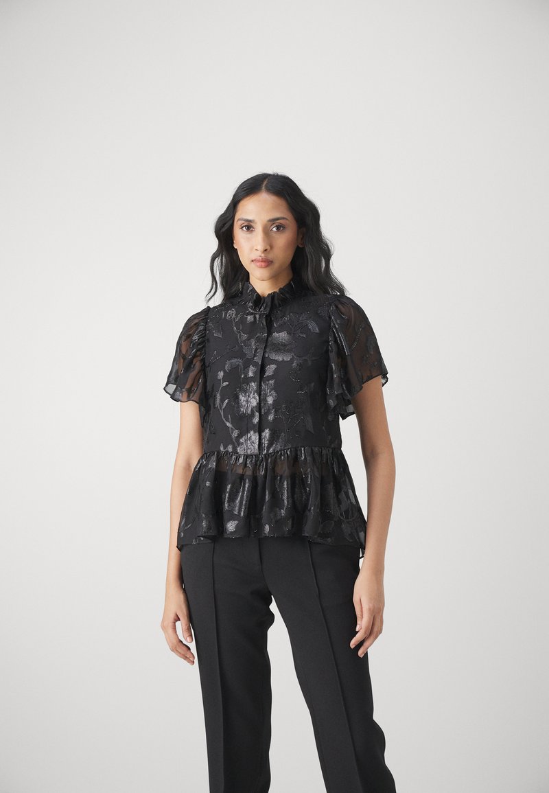 Schwarze Peplum-Bluse mit rüschengerüschten kurzen Ärmeln, floralem Muster, strukturiertem Stoff und hohem Kragen. Kombiniert mit schwarzen Hosen.