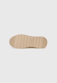 Light tan rubber outsole featuring horizontal grooves for traction and embossed branding. Smooth surface with rounded edges.
