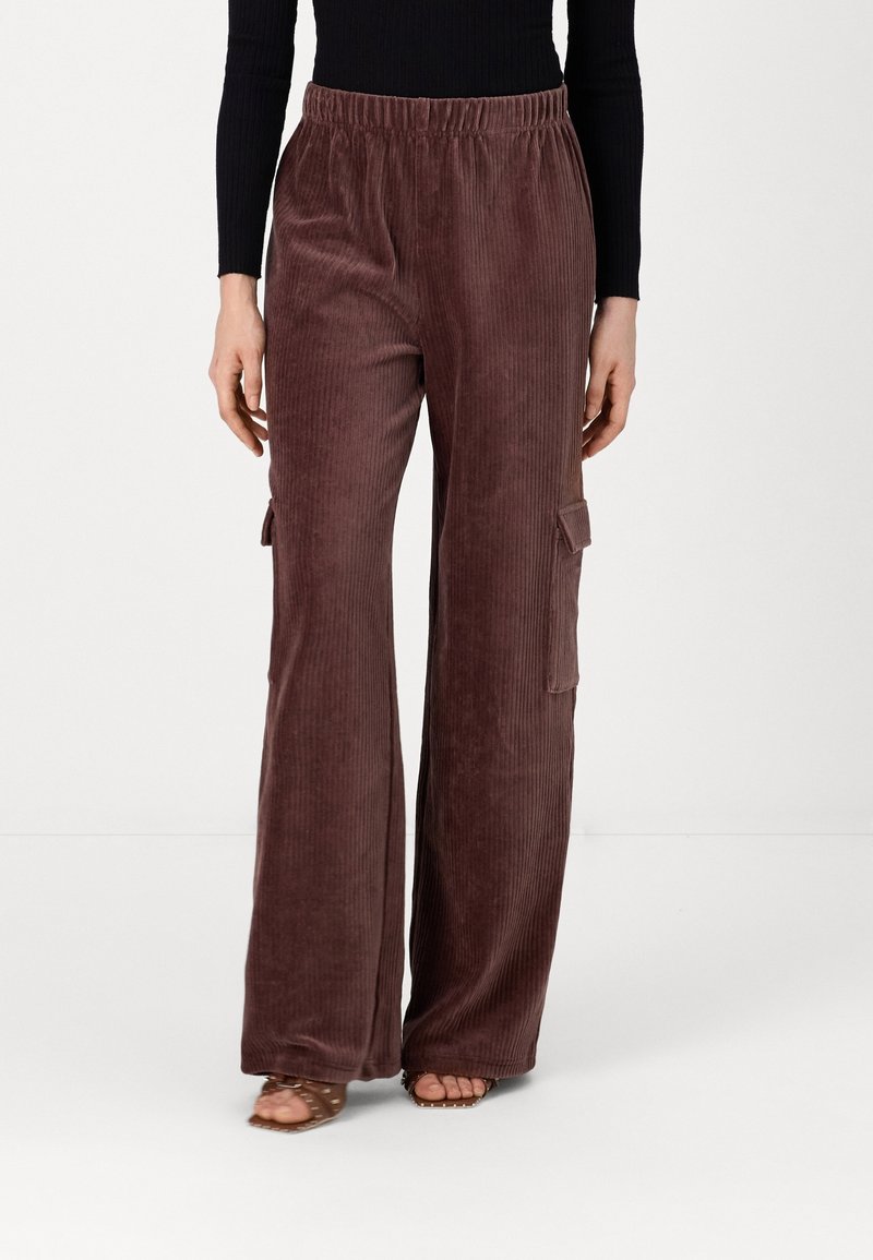 Pantalon large en velours côtelé marron avec une taille élastique et des poches cargo latérales, présentant une texture douce et des côtes verticales.