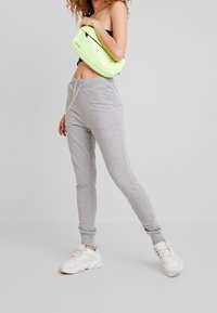 Grå sweatpants med dragsko i midjan, smalnande ben och sidofickor. Parat med vita sneakers och en neongrön axelväska.