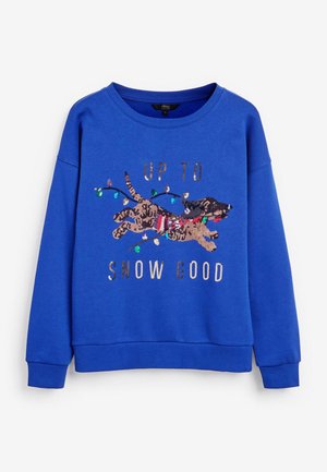 Modrá mikina s flitrovým jezevčíkem, který má na sobě proužkovanou šálu a vánoční světýlka, na mikině je nápis „Up to Snow Good.“