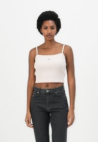 Pink ribbed cropped top with thin straps and a small logo detail on the front, paired with high-waisted black jeans.