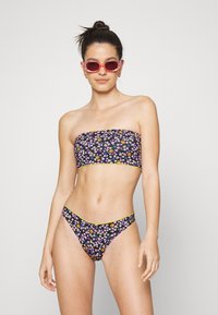 Conjunto de biquíni floral com topo sem alças e parte de baixo de cintura baixa. Base preta com flores multicoloridas e acabamento amarelo. Textura suave.