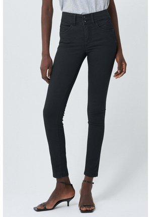 Czarne, dopasowane jeansy z wysokim stanem, noszone z czarnymi, odkrytymi sandałami na obcasie z paskami oraz włożonym do spodni jasnoszarym topem, prezentowane na stojącej modelce.