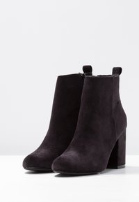 Stivaletti alla caviglia in corduroy nero con tacco spesso, caratterizzati da una texture liscia e chiusura con zip, progettati con linguette posteriori per facilitarne l'indossamento.
