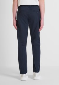 Pantaloni in cotone blu navy con vestibilità slim, due tasche posteriori con bottoni e orlo a coste, abbinati a sneakers bianche.